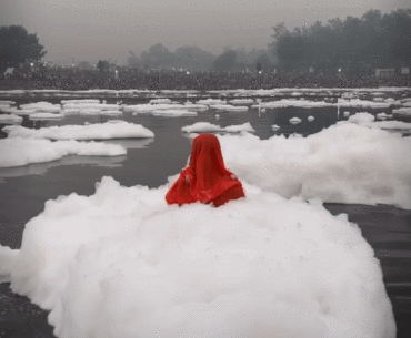 Woman praying in Yamuna river as toxic foam floats over her