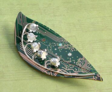 Brooch with hand forged fine silver lily of the valey flowers on a sterling stem. The leaf is a polished and sealed circuit board inlaid with opals.