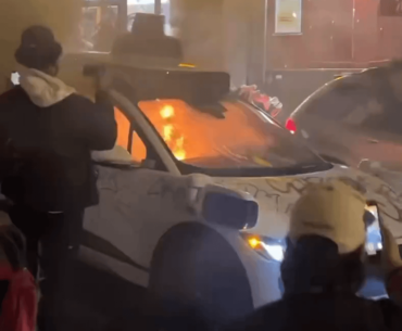 Autonomous vehicle destroyed by protestors in high tech city with Kanji in the background