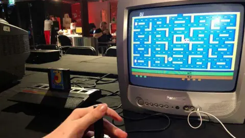 BBC Image shows hand at the controls of an Atari game console playing Pac-Man on a Panasonic television