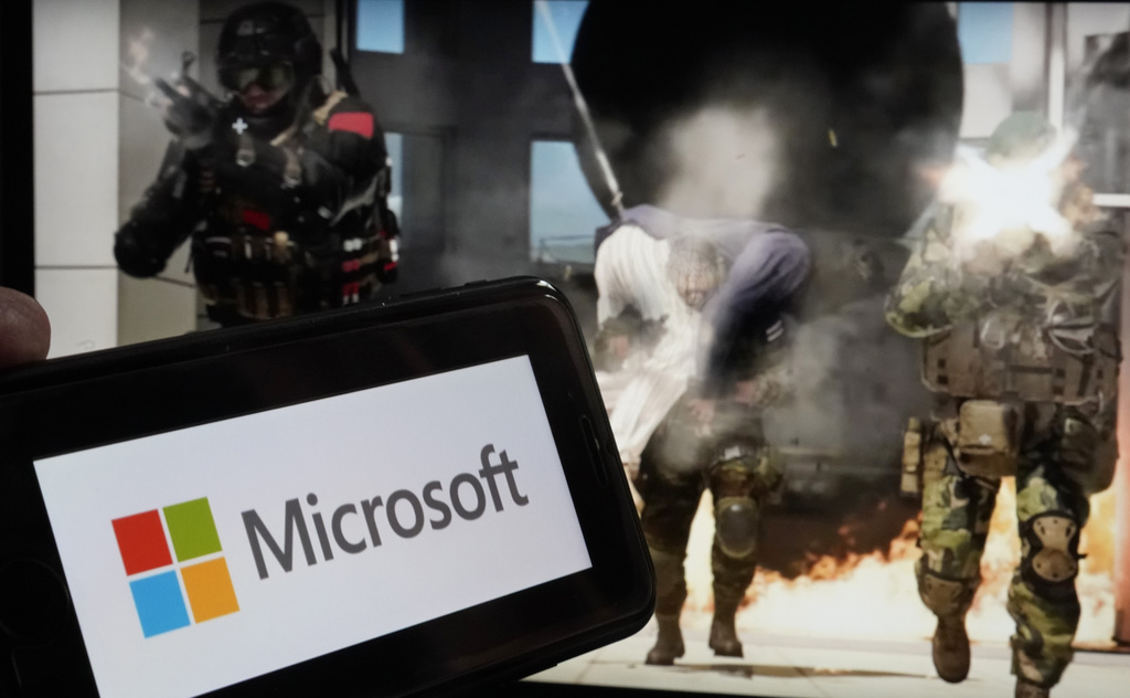 Wisconsin video game developer hit with layoffs amid larger Microsoft cuts A smartphone displaying the Microsoft logo is held in front of a screen showing armed soldiers and an explosion in an action scene.