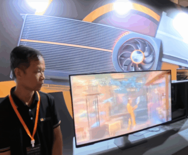 Expo booth with GPU display, screen showing graphics, and two attendees with lanyards.