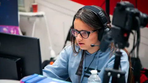 Getty Images Thibaut Durand Shows a girl in a blue hoodie, glasses and headset with mic playing a computer game