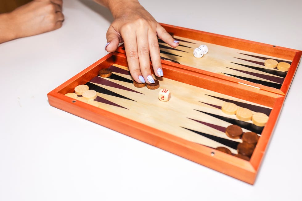 close up of female hand with light blue nail polish moving two pieces on a backgammon board close up of female hand with light blue nail polish moving two pieces on a backgammon board