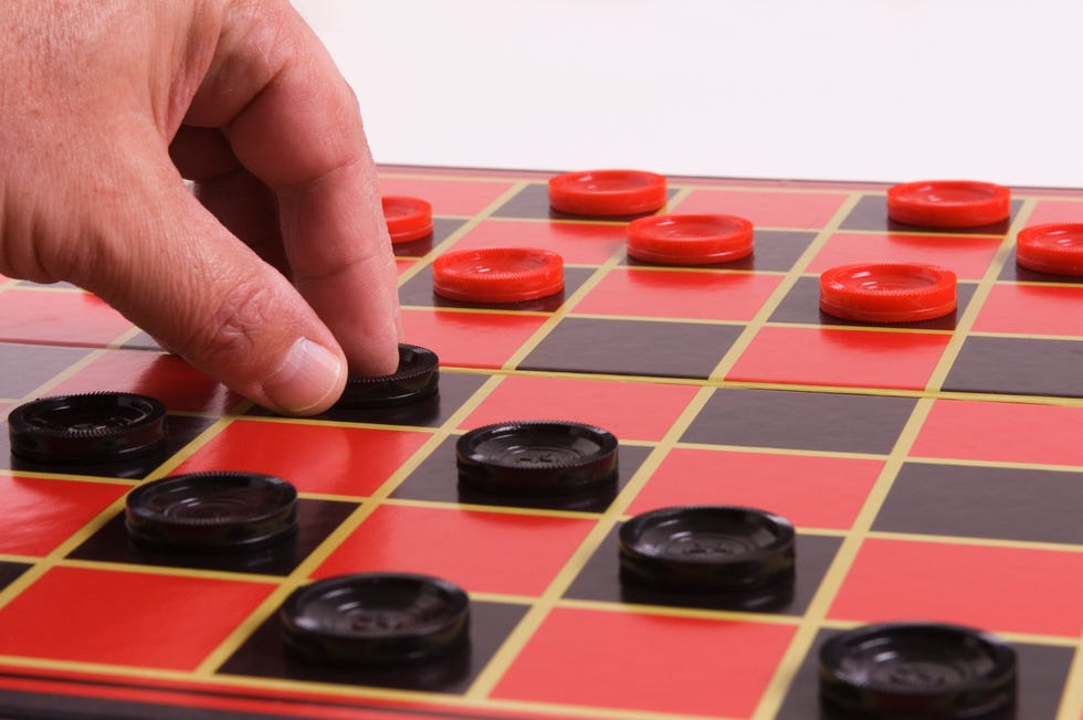 a man's hand moving a black piece on a black and red checkers board a man's hand moving a black piece on a black and red checkers board