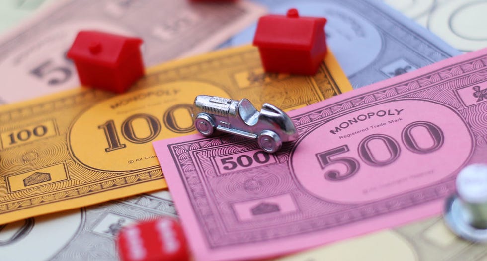 colorful play money with red plastic houses and a silver car game piece on a monopoly board colorful play money with red plastic houses and a silver car game piece on a monopoly board