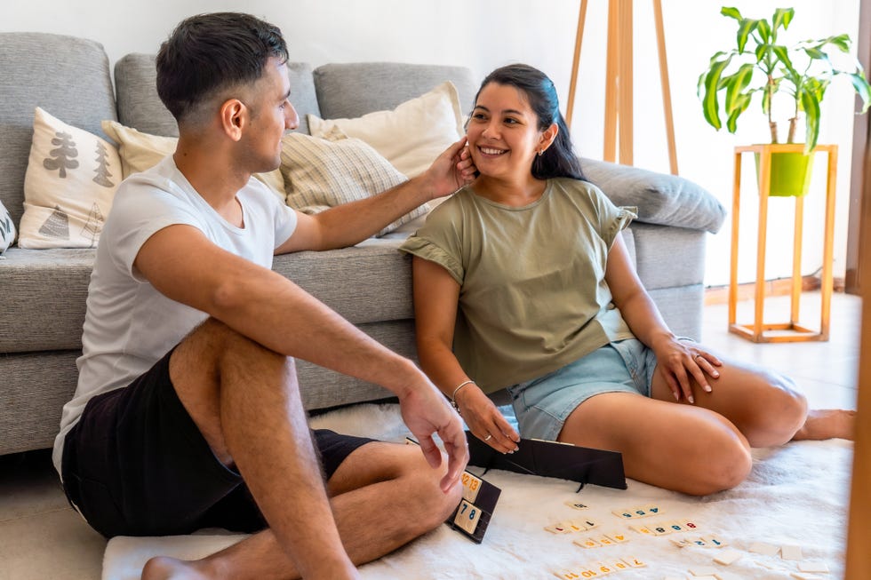 happy latin couple enjoying a lively game of rummy on a white carpet in their cozy living room, sharing smiles and playful moments happy latin couple enjoying a lively game of rummy on a white carpet in their cozy living room, sharing smiles and playful moments