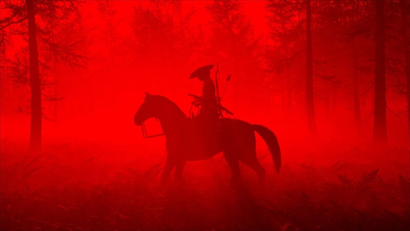 A lone rider on horseback carries a bow and wears a hat, silhouetted against a vivid red, misty forest with tall trees in the background.