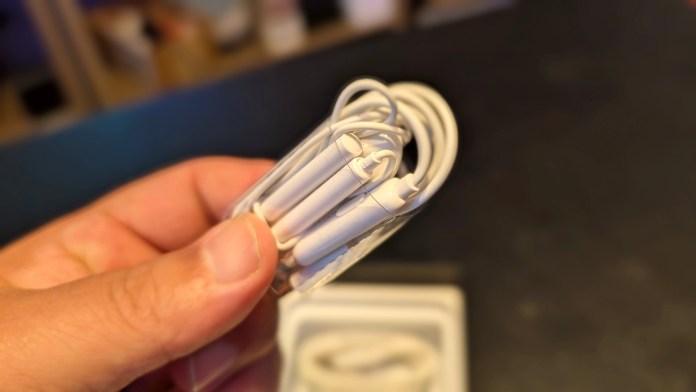 Close-up of a hand holding a pair of white wired earbuds, with the background slightly blurred.