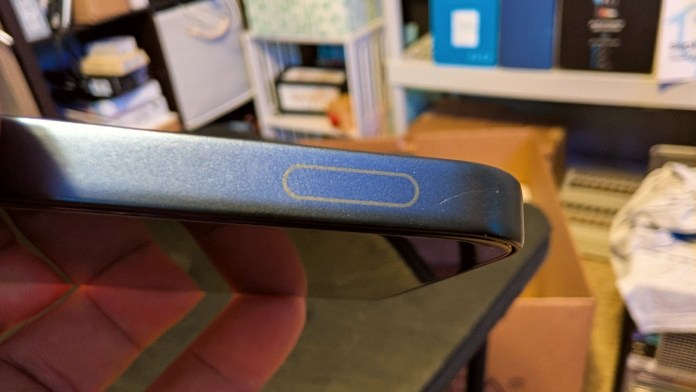 Close-up view of the side of the Infinix GT 30 smartphone, showcasing the power button, with a hand holding the device. The background features storage bins and boxes.