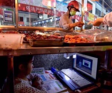 Chinese kid taking online class under her parents’ street food stand.