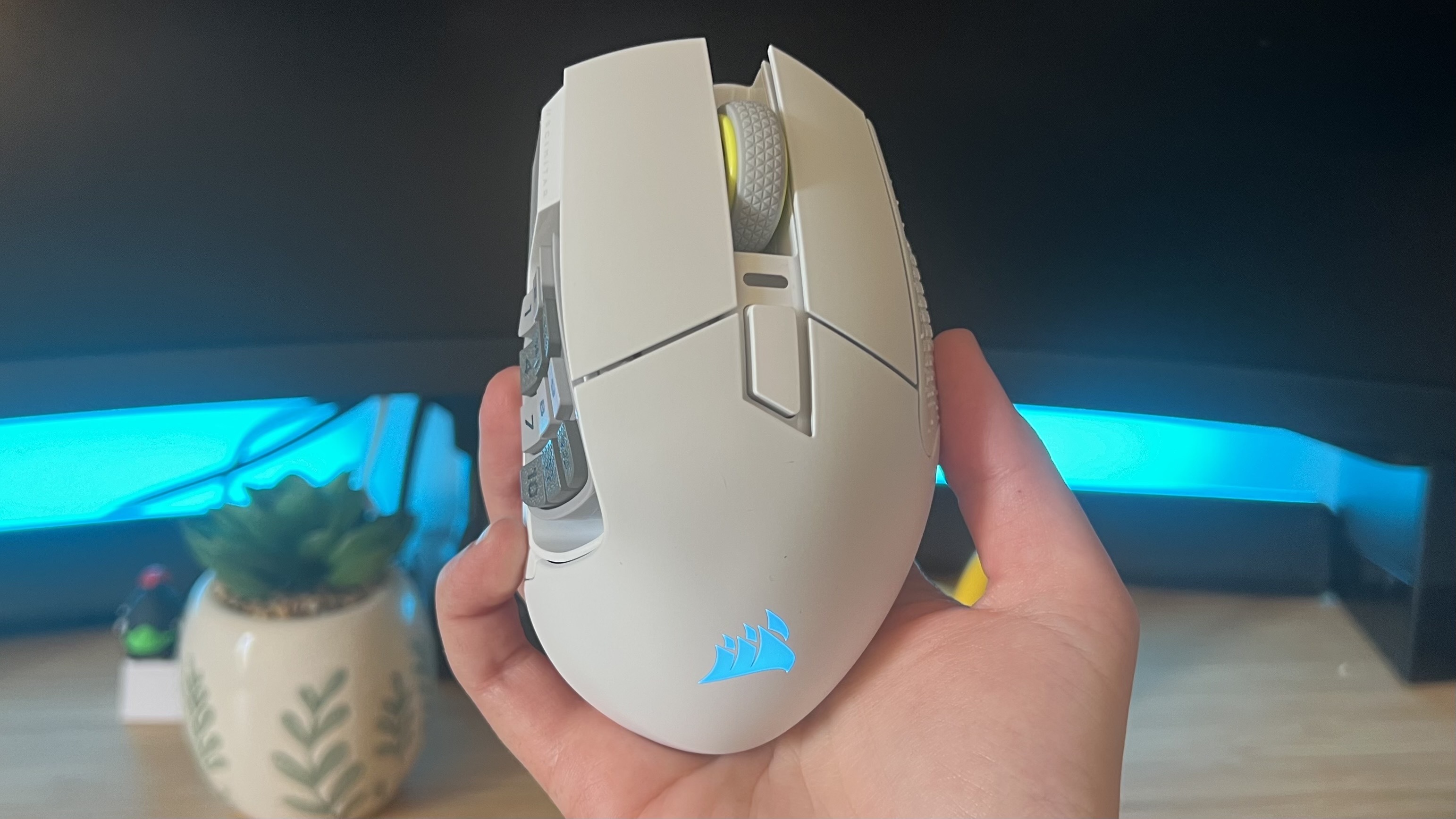 Corsair Scimitar Elite Wireless SE gaming mouse held in a hand against a gaming setup