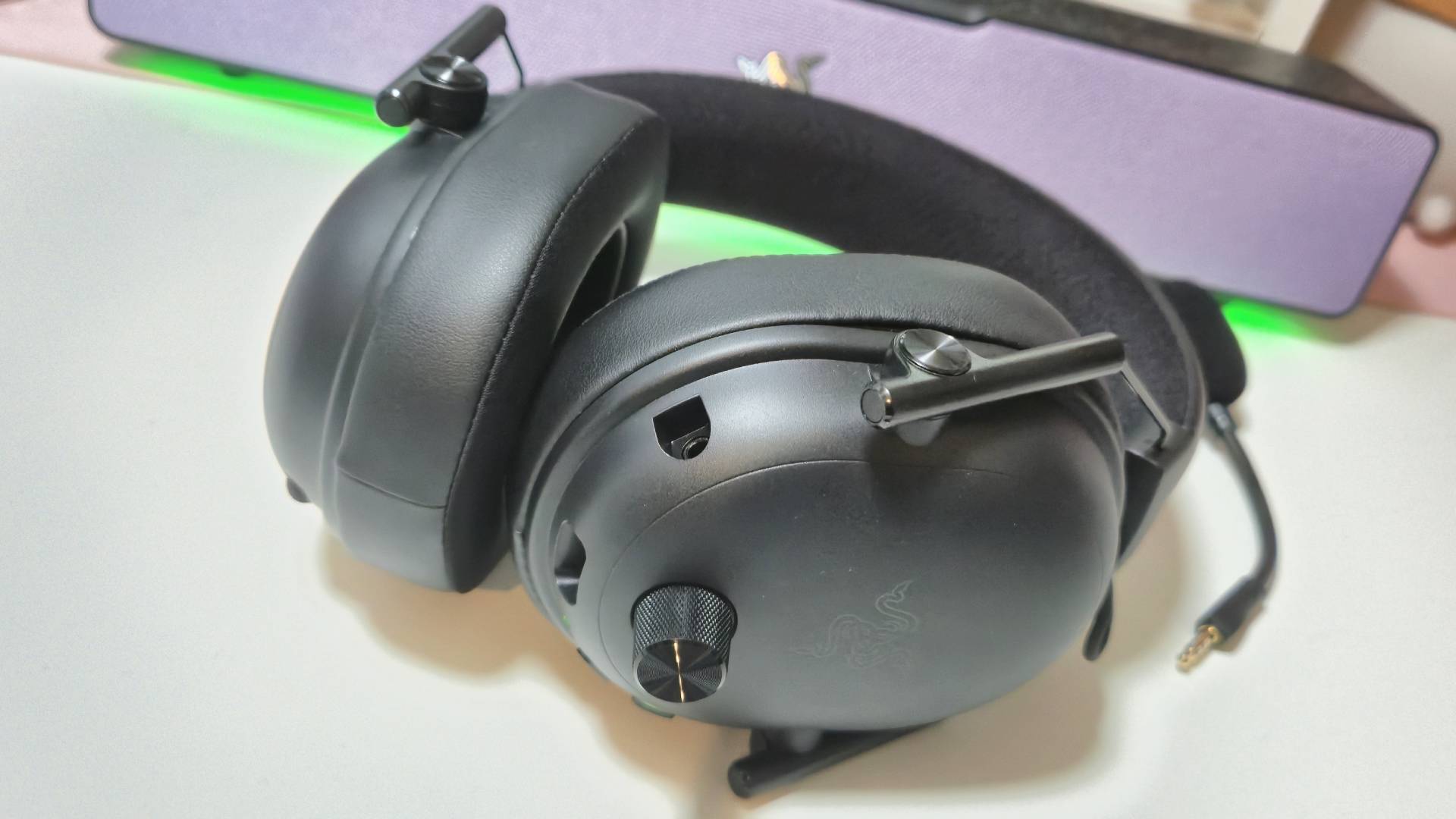 Photo of the Razer BlackShark V3 sitting on a white desk with a green glow behind it.