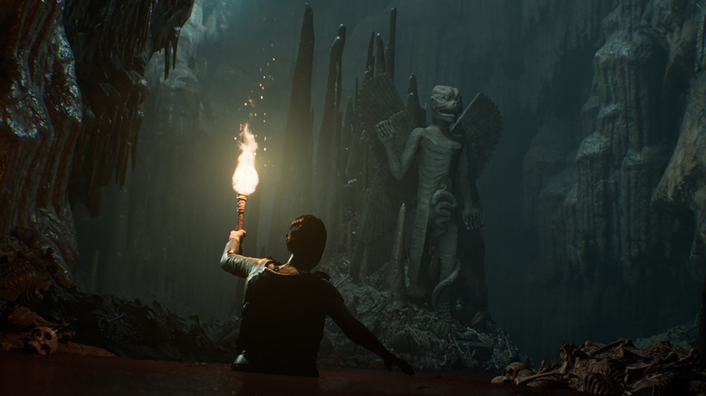 Rachel King wades through water with a lit torch toward a demonic statue in 