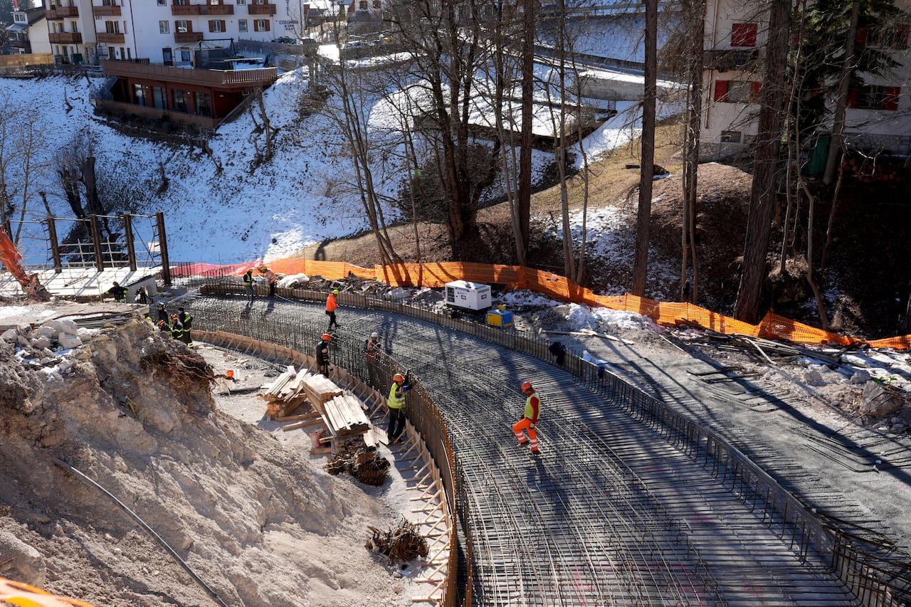 Construction workers stand on a luge track that's under construction.