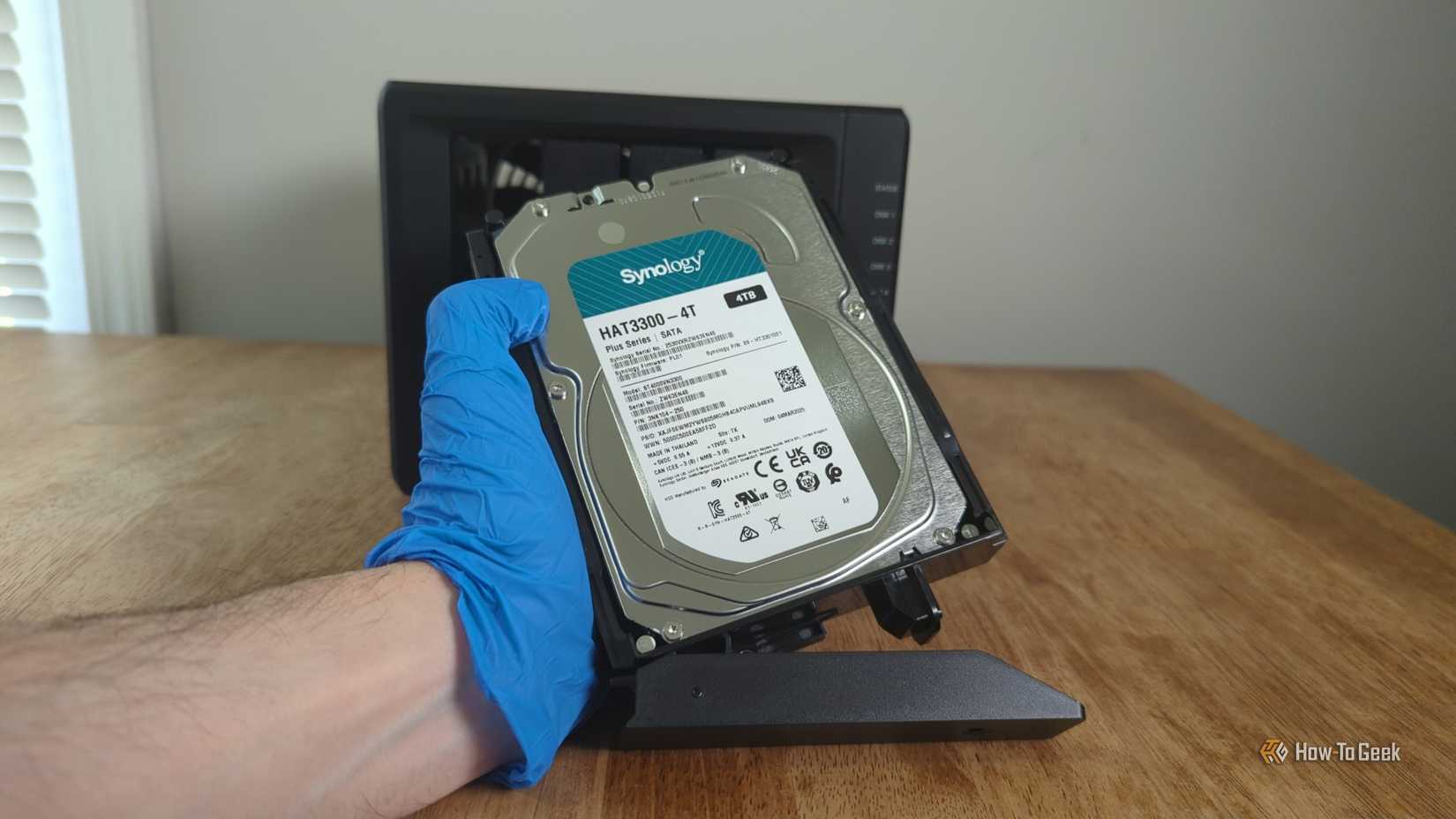 Person's gloved hand holding a Synology HDD in front the Synology DS425+ NAS.-2
