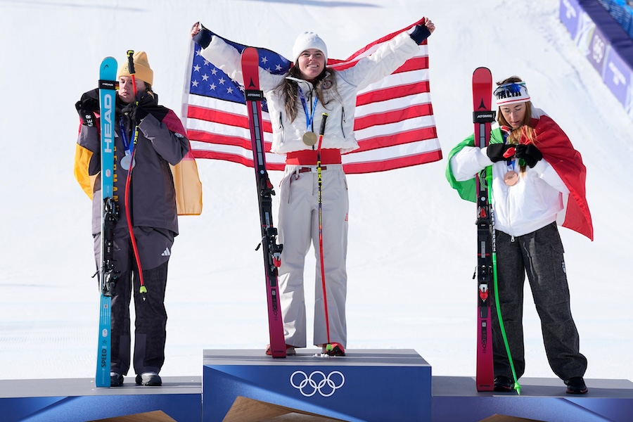 United States' Breezy Johnson, center, gold medal in an alpine ski women's downhill race, celebrates on the podium with silver medalist Germany's Emma Aicher, left, and bronze medalist Italy's Sofia Goggia, at the 2026 Winter Olympics, in Cortina d'Ampezzo, Italy, Sunday, Feb. 8, 2026. 