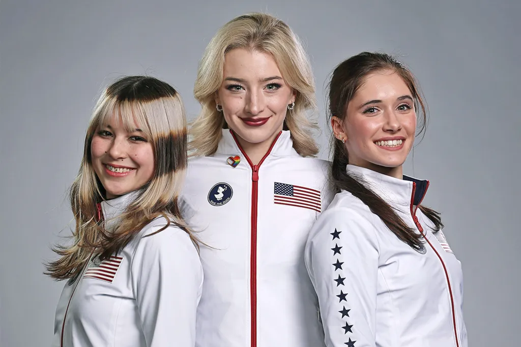 Three athletes wearing white Team USA jackets stand side by side and smile at the camera.