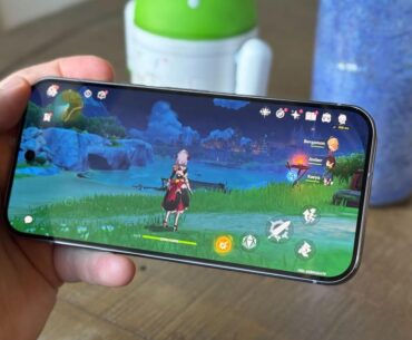 A smartphone playing an adventure game, Genshin Impact, in front of a table background.