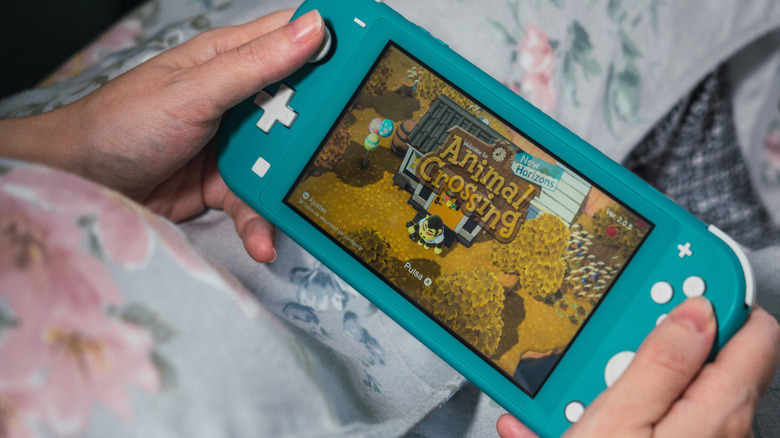 Hands holding a Nintendo Switch Lite displaying Animal Crossing: New Horizons on the screen.