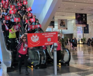 Members of the Game Workers United-CWA union ride down an escalator at GDC 2026 holding red banners that read "We're stronger together"