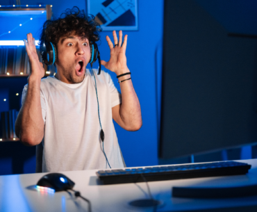 Shocked young arabic gamer wearing headphones screaming playing video game on personal computer, play in eSport cyber games tournament in neon light.