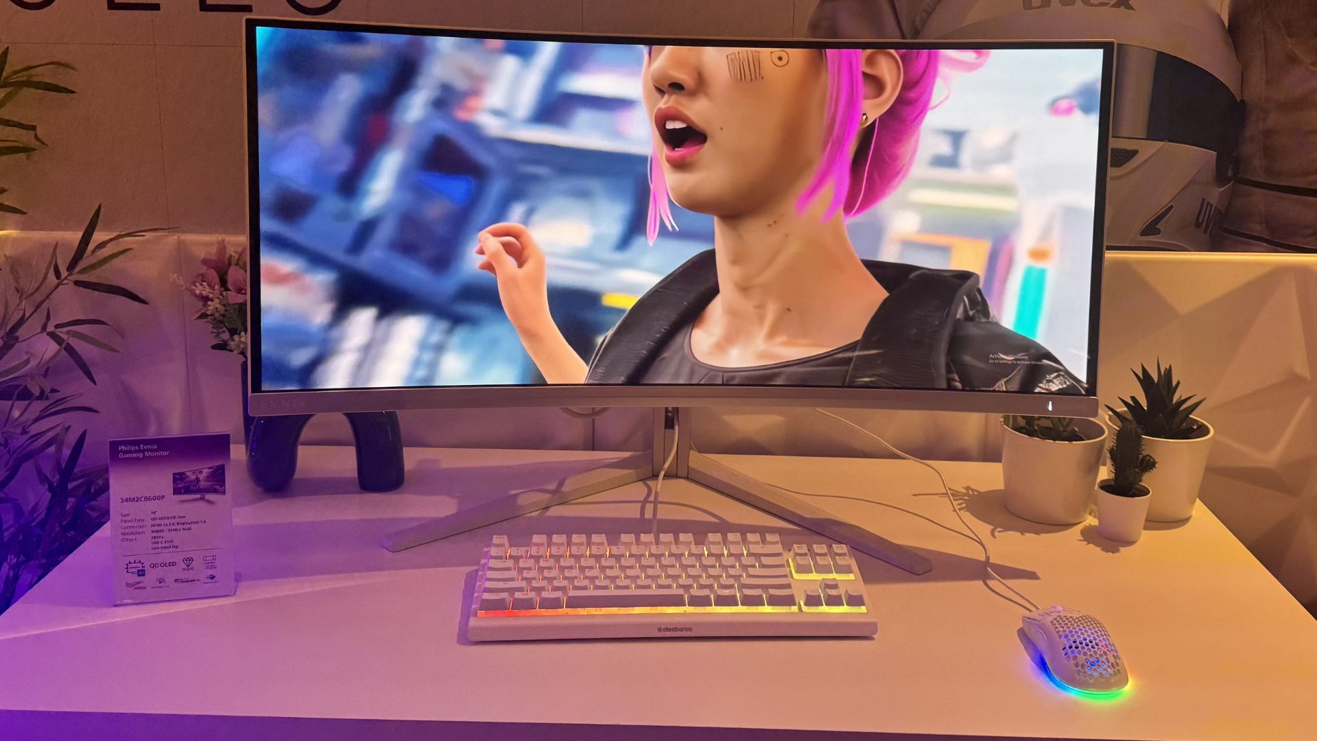 Philips Evnia 34M2C8600P gaming monitor on a white desktop, showing a woman with pink hair