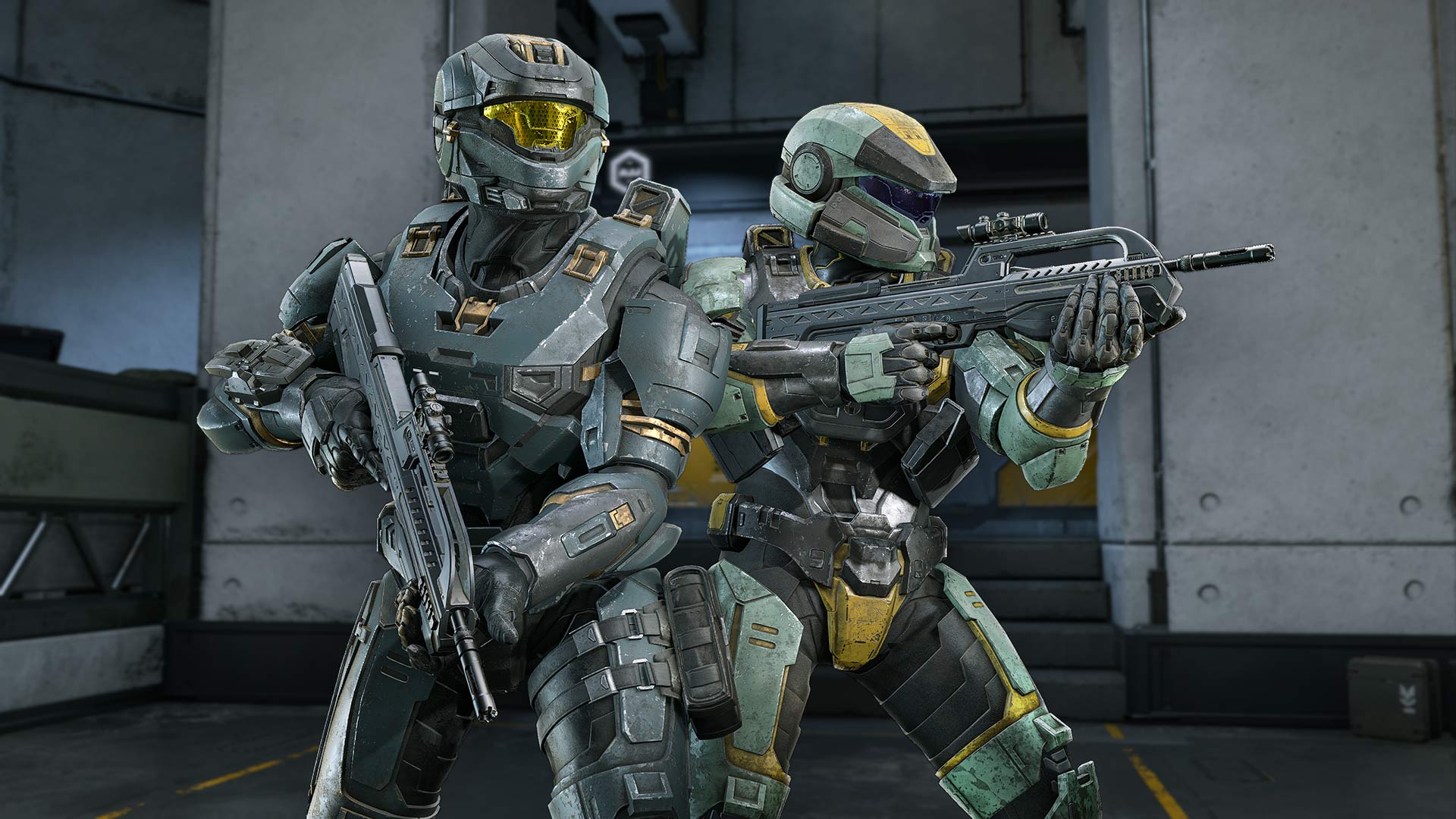 Two Spartan soldiers stand back-to-back in Halo Infinite, holding rifles inside a futuristic facility.