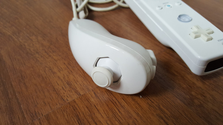 A Nunchuk, attached to a Wii Remote, on a wooden surface