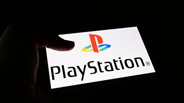 A mobile phone in a dark room showing the PlayStation logo on the screen