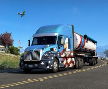 A virtual semi-truck with an American flag design on a highway, with a house, car, and airplane in the gameplay scene of American Truck Simulator.