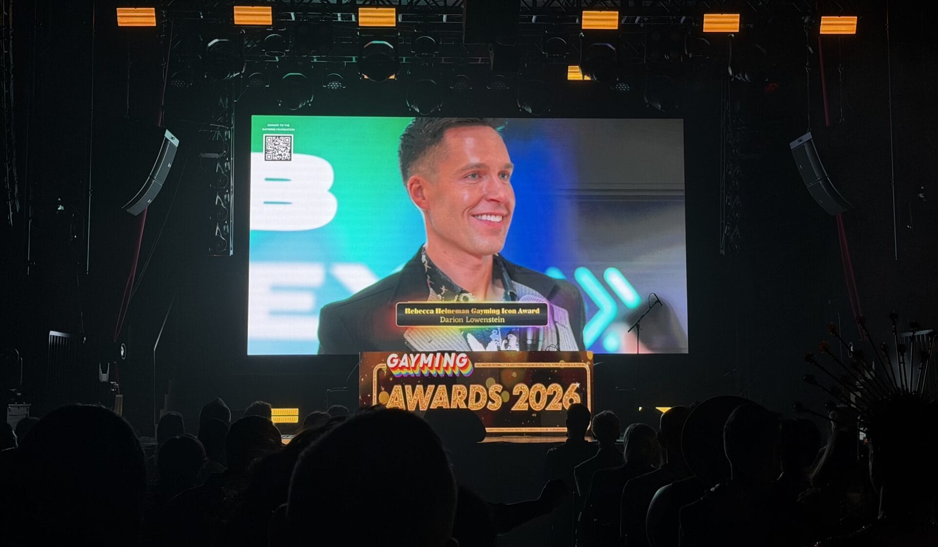 darion GA2026 | GLAAD Smiling man on a large stage screen during an awards ceremony, with a colorful backdrop and the text 'GAYMING AWARDS 2026' visible at the bottom.
