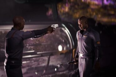 A scene from the game Directive 8020 showing two characters in a tense standoff, with one character aiming a gun at the other who holds a staff, set against a futuristic background.