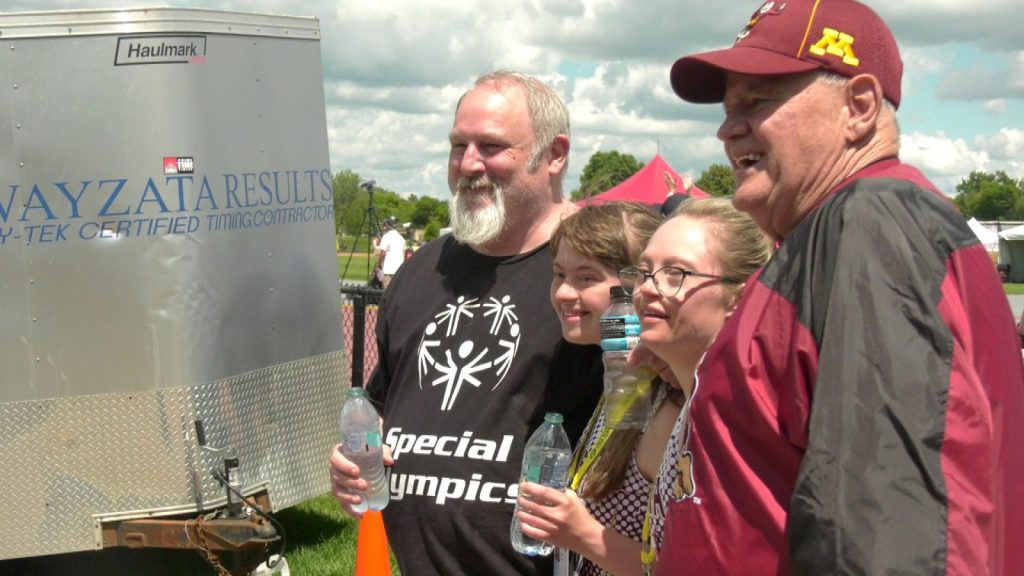 four people smile for a photo, the two young women in the middle wear minnesota track uniforms