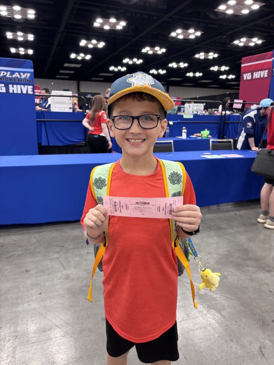 A boy stands holding a pink piece of paper