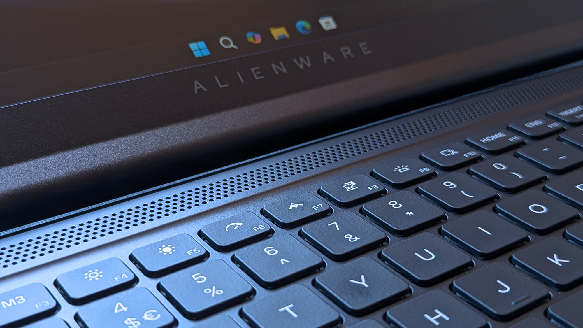 A close-up of an Alienware laptop shows the &ldquo;ALIENWARE&rdquo; branding above the keyboard, with visible function keys, number keys, and part of the Windows taskbar on the screen.