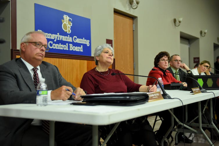 Five people sit in front of a sign that reads