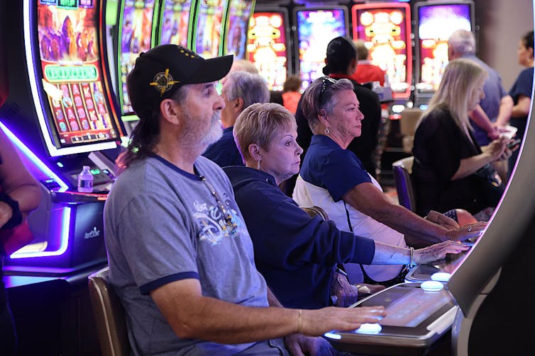A man and two women sit behind gaming machines.