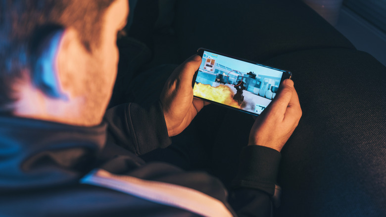 a person holding a smartphone while gaming on it in landscape mode