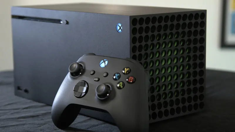 An Xbox Series X console and controller are displayed on a table. The console is black and rectangular, with the controller in the foreground.