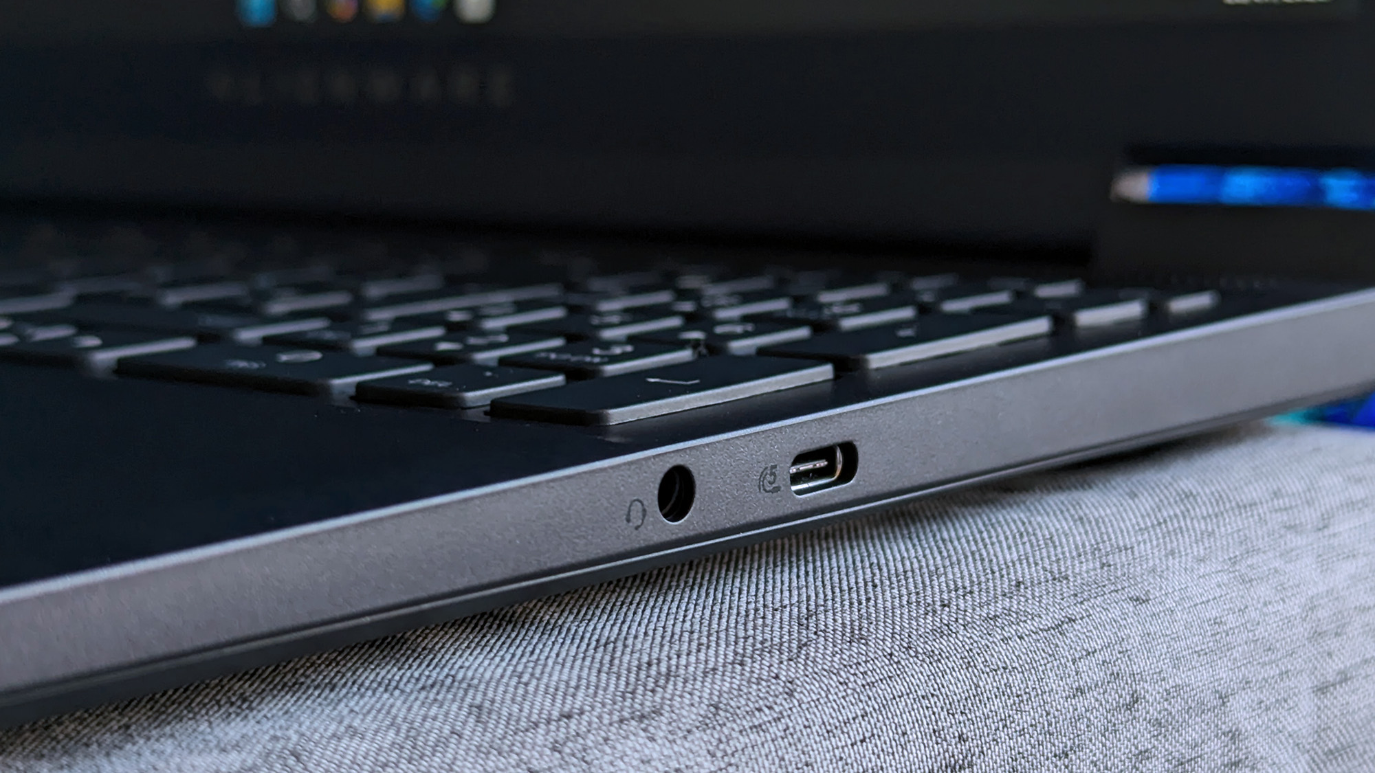 A close-up of an Alienware 15 laptop’s right side shows a 3.5mm headphone jack and a USB‑C port, with part of the keyboard and faint Alienware branding visible on the bezel.