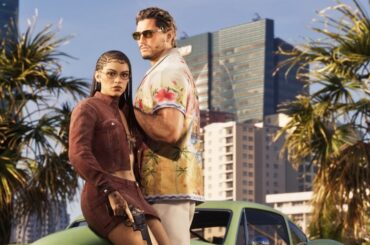 Screenshot from Grand Theft Auto 6. Jason Duval and Lucia Caminos stand together in front of palm trees and a modern cityscape. Lucia wears a cropped rust-colored jacket and glasses, with her hair in braids. Jason, wearing sunglasses and a tropical-print shirt, stands slightly behind and to her right.