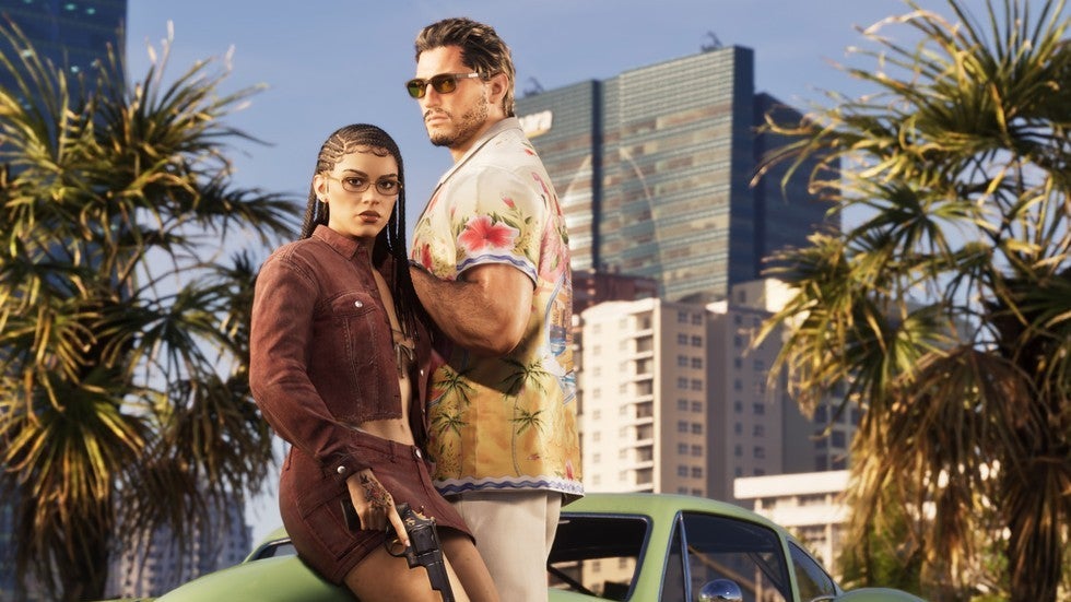 Screenshot from Grand Theft Auto 6. Jason Duval and Lucia Caminos stand together in front of palm trees and a modern cityscape. Lucia wears a cropped rust-colored jacket and glasses, with her hair in braids. Jason, wearing sunglasses and a tropical-print shirt, stands slightly behind and to her right.