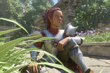 Enshrouded player character with red hair in silver knight-like armor sitting on a stoney path with flowers